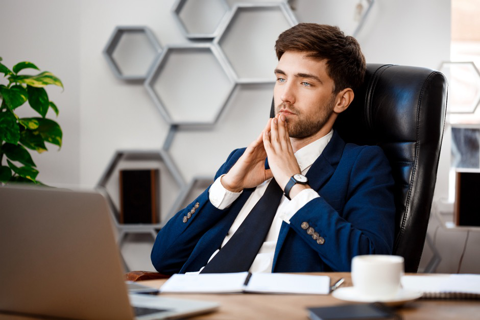 A male executive calmly sits at his desk looking thoughtful.