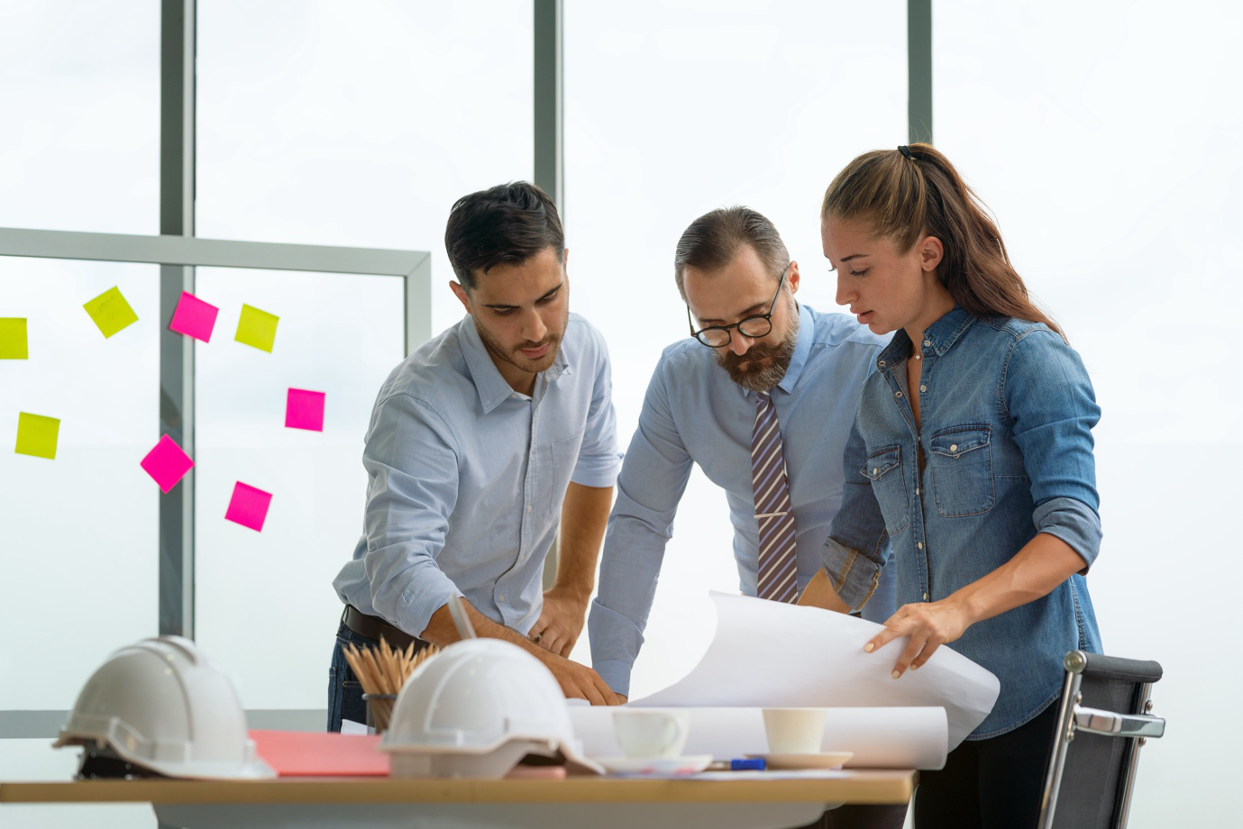 Engineers reading a blueprint in an office, discussing project details.