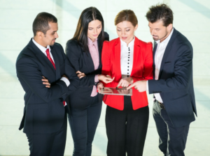 Two men and two women dressed in business attire collaborating over a tablet