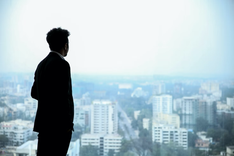 An entrepreneur in a black suit standing at a window and looking at the city