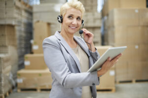 a woman supply chain recruitment manager wearing wireless headphone holding an iPad in a warehouse