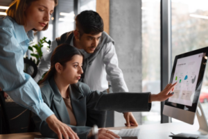 a woman points at a computer screen with graphs while her colleagues look on