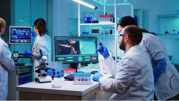 a scientist holds up a sample of a red liquid with a computer in the background